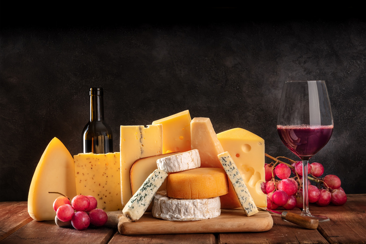 Cheese and wine. An assortment of various cheeses with a wineglass and a bottle, side view on a black background with a place for text