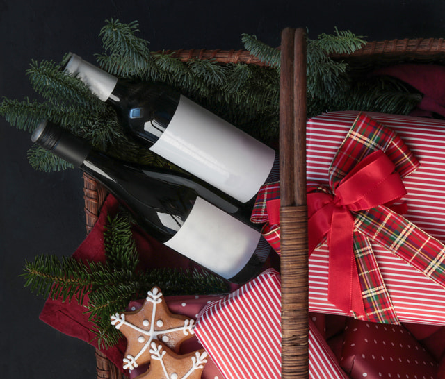 Holiday gift basket with wine bottles, wrapped gift and gingerbread cookies.